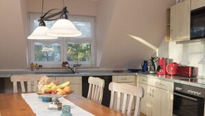 Uma cozinha com mesa de madeira, cadeiras, um cesto de frutas e uma cafeteira.
