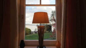 Una ventana con una lámpara en el alféizar, un florero y vistas a un lago y vegetación.