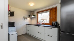 A compact kitchen with white cabinets, a built-in microwave, a refrigerator, and a window with a view of the outside.