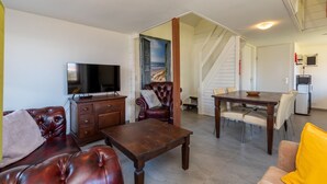 A living room with a TV, leather sofa, wooden coffee table, and a dining area with a table and chairs.