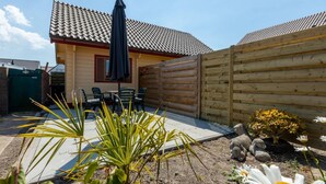 A small house with a tiled roof, a patio with chairs, and a wooden fence.