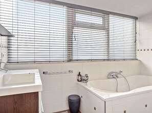 Une salle de bain moderne avec une grande baignoire, un lavabo et une fenêtre équipée de stores.