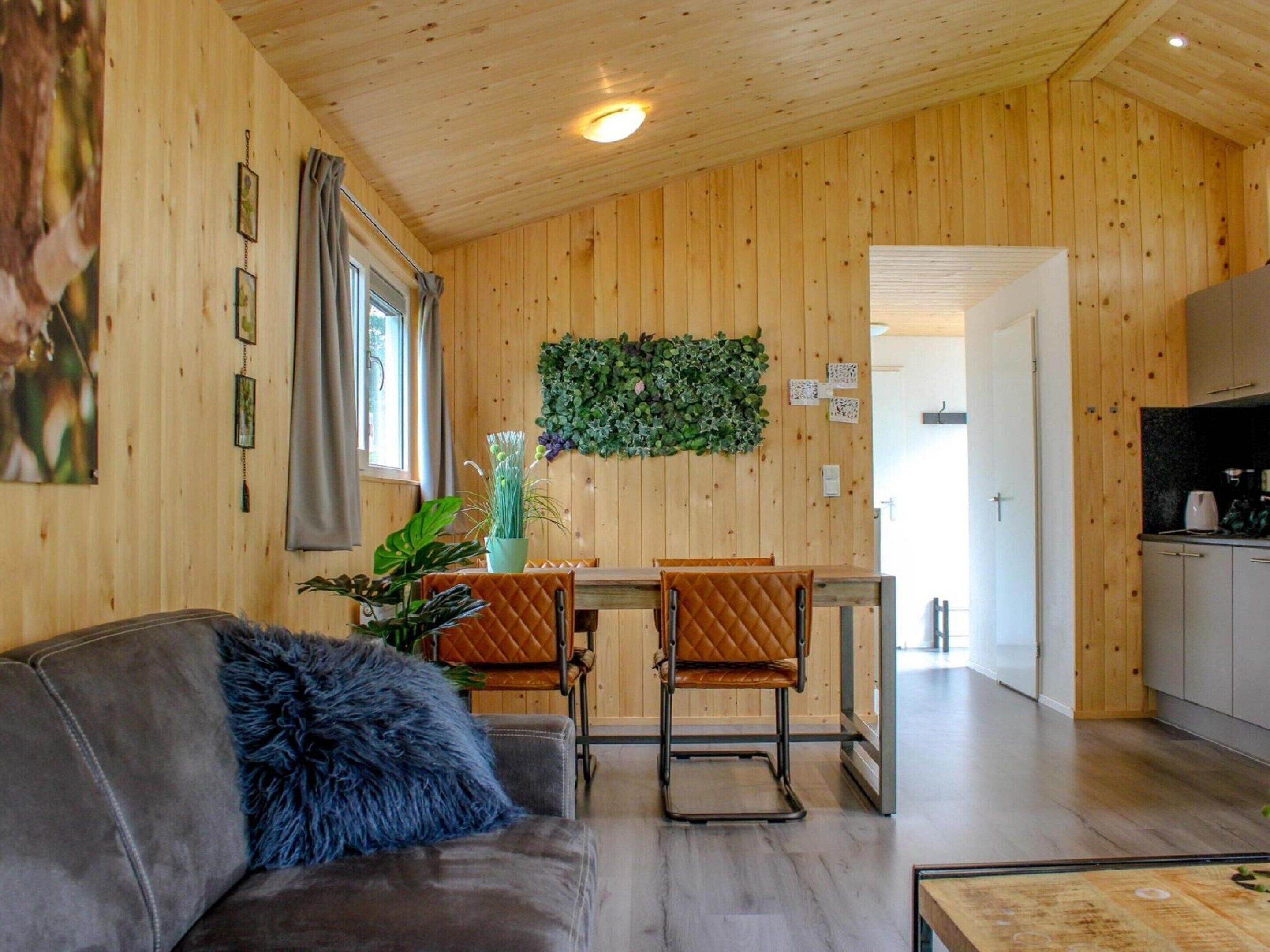 A cozy cabin interior with a wooden interior, a dining area with a table and chairs, a sofa with a fluffy pillow, and a kitchen area.