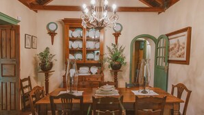Une salle à manger avec une table en bois, des chaises, un lustre et un buffet où sont exposées des assiettes.