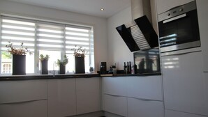 A modern kitchen with white cabinets, a built-in oven, and a window with blinds. - Modern Holiday Home With Veranda in Limmen (Limmen)