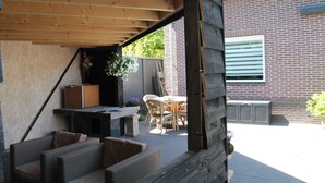 An outdoor patio area with wicker furniture, a table, and a hanging flower arrangement. - Modern Holiday Home With Veranda in Limmen (Limmen)
