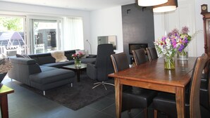 A modern living room with a sofa, coffee table, and dining table. There is a fireplace, a TV, and a clock on the wall. - Modern Holiday Home With Veranda in Limmen (Limmen)