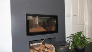 A modern fireplace with a TV screen, a log storage area, and a potted plant. - Modern Holiday Home With Veranda in Limmen (Limmen)