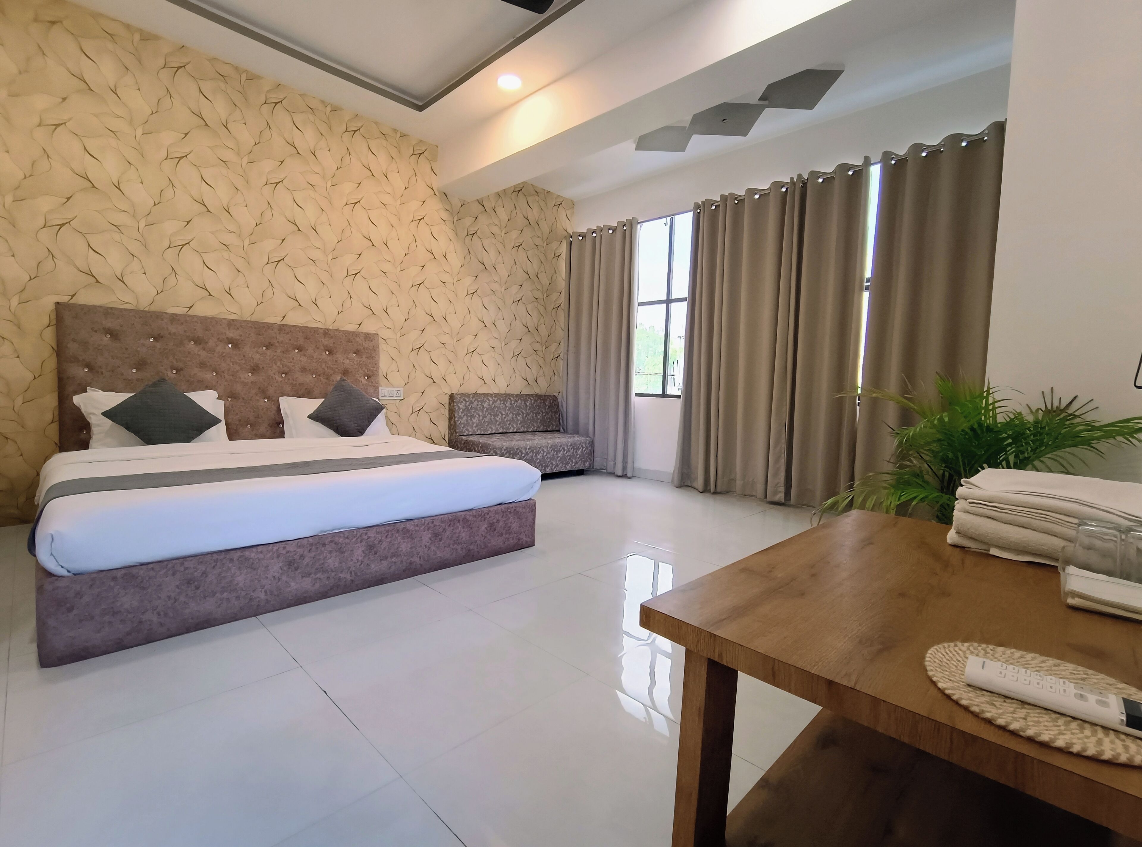 A hotel room with a large bed, a small sofa, a wooden table, and a window with curtains.