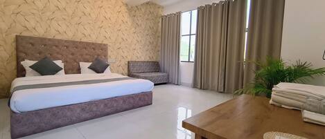 A hotel room with a large bed, a small sofa, a wooden table, and a window with curtains.