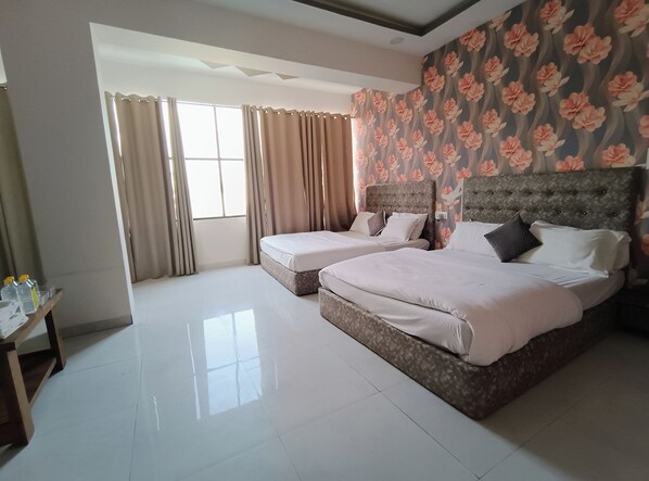 A hotel room with two beds, a large window with curtains, a floral wallpaper, and a tiled floor.