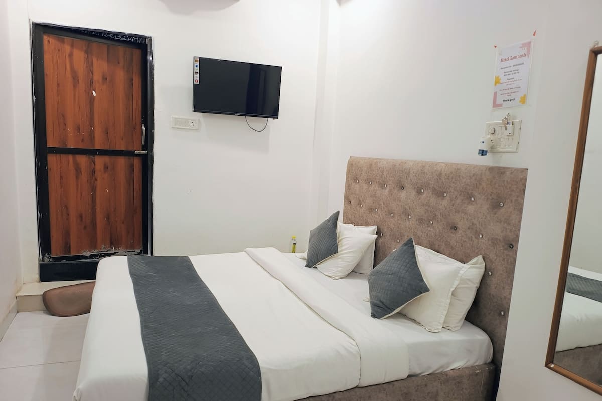 A bedroom with a bed, a television, a wooden door, and a mirror.