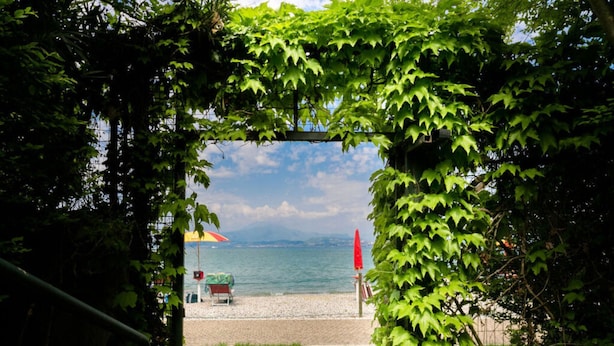 Ein Sitzbereich im Freien mit Blick auf das Meer, einem roten Sonnenschirm und einer Bank.