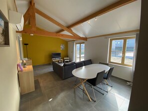 A modern living room with a sofa, a dining table with chairs, a TV, and a window with a view of the beach. - Holiday Home Near Sint-andre Beach (Koksijde)