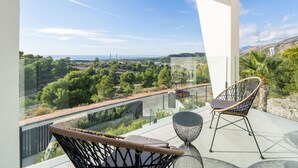 Un balcone con sedie in vimini e un tavolino, affaccia su un paesaggio pittoresco con alberi e una vista lontana di un ponte.