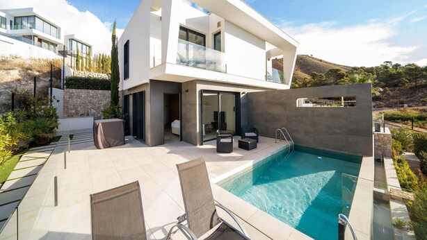 Una moderna casa a due piani con piscina, area relax esterna e un muro in pietra.