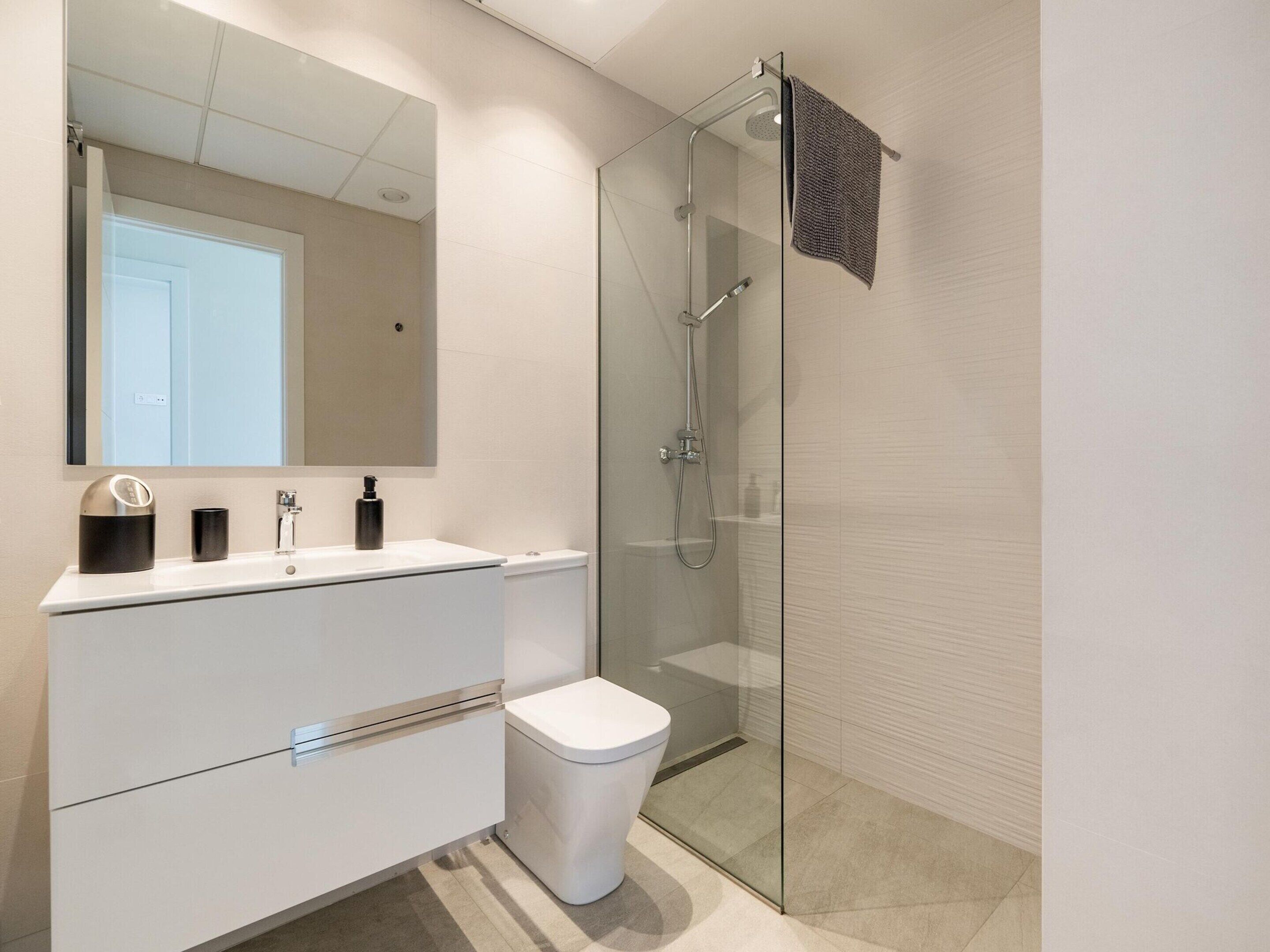 Ein modernes Badezimmer mit einer gläsernen Duschkabine, einem weißen Waschtisch mit Spiegel und einer Toilette.