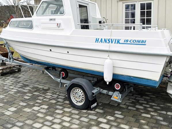 A white boat named 'HANSVIK 18 COMBI' on a trailer with a house in the background.