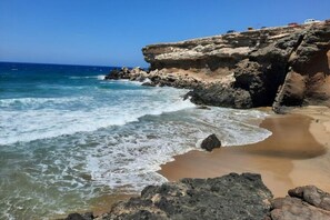 Litoral rochoso com ondas quebrando na praia.