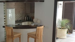 A kitchen with a dark countertop, two wooden bar stools, and a potted plant. - Bungalow Villa del Sol (Pajara)