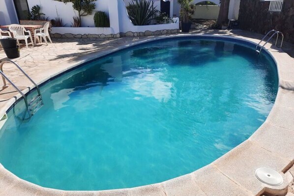 Piscina azul límpida com um deck de pedra, rodeada por paredes brancas e plantas em vasos.