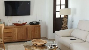 A living room with a wooden cabinet, a glass coffee table, a beige sofa, a television mounted on the wall, and a lamp beside the sofa. - Bungalow Villa del Sol (Pajara)