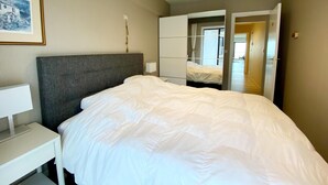 Quarto de hotel com cama grande, mesa de cabeceira, guarda-roupa e espelho.