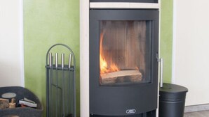 A wood-burning stove with a glass door, a metal grate, and a black chimney. - Fereienhaus Mellumplate (Wurster Nordseeküste)