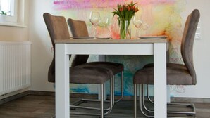 A dining area with a white table, four brown chairs, and a colorful abstract mural on the wall. - Fereienhaus Mellumplate (Wurster Nordseeküste)