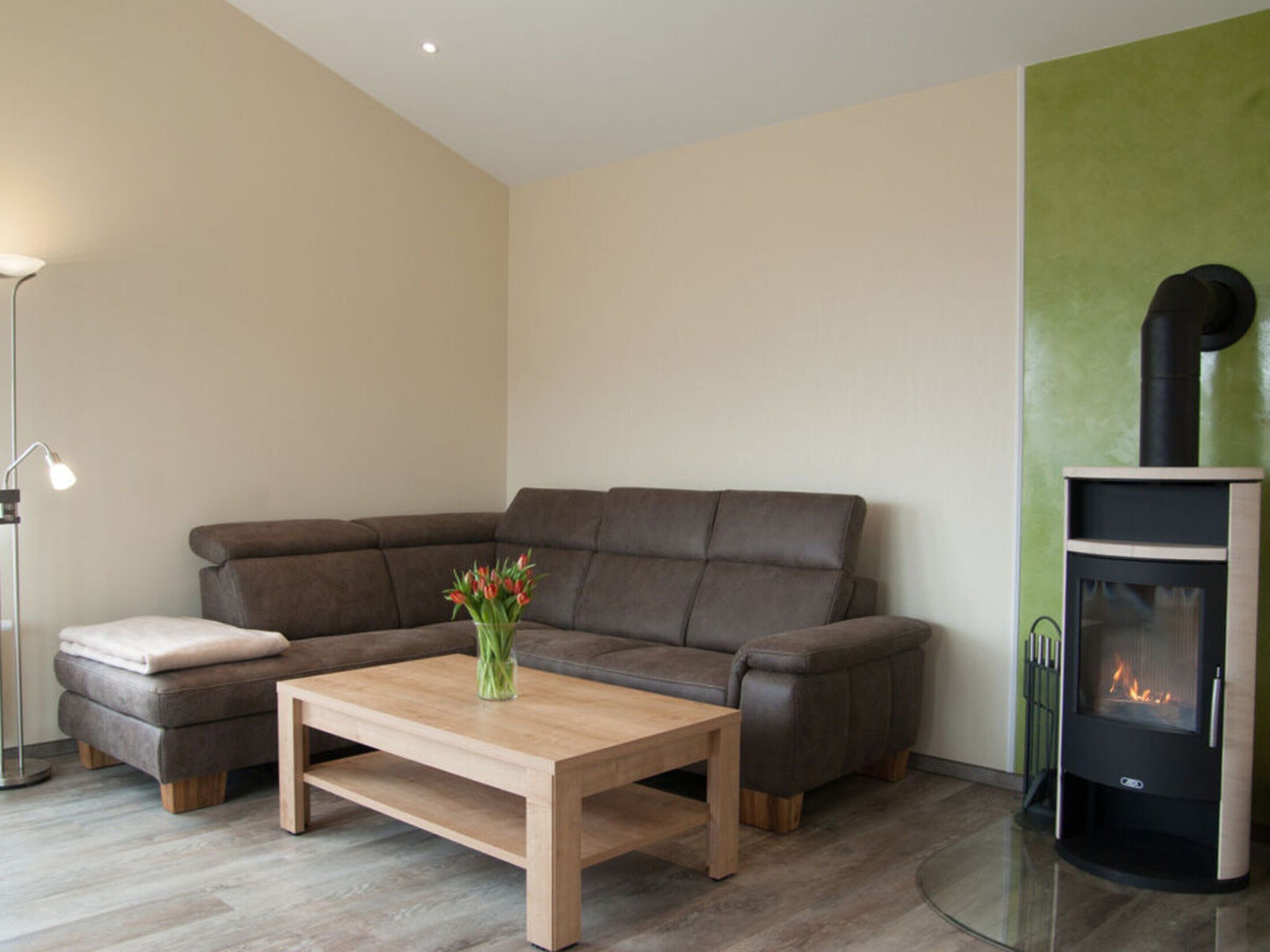 A modern living room with a sectional sofa, a wooden coffee table, a floor lamp, and a wood-burning stove.