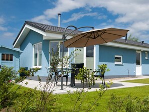 Une maison à deux étages avec une façade bleue, une terrasse dotée de meubles d’extérieur et d’un grand parasol.