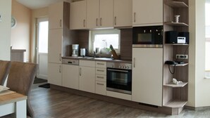 A modern kitchen with white cabinets, a built-in oven, and a microwave. - Fereienhaus Mellumplate (Wurster Nordseeküste)