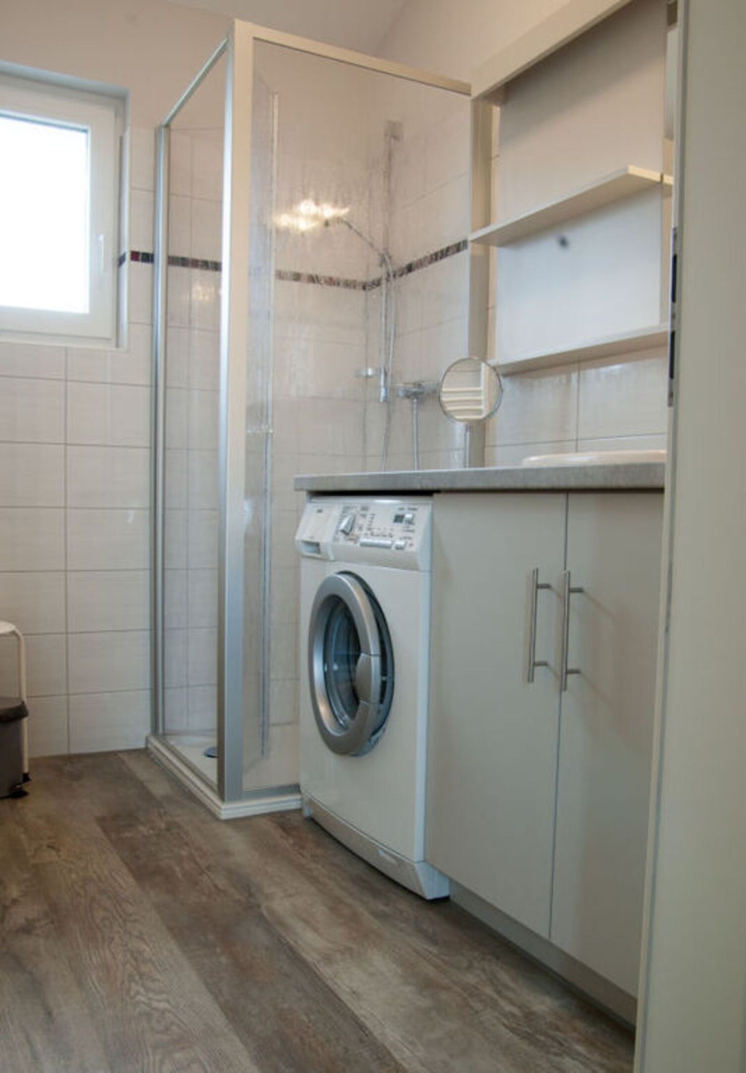 A compact laundry area with a washing machine, a glass shower enclosure, and a tiled shower wall.