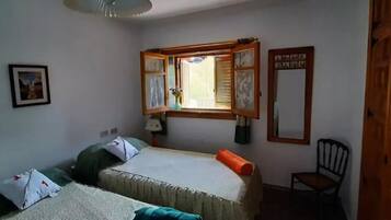 Una habitación con dos camas individuales, una ventana con marco de madera, una silla y una mesita.