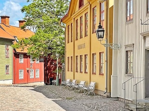 A cobblestone street with a yellow building, red and green buildings, and a row of white benches. - 4 Person Holiday Home in Gusum (Valdemarsvik)