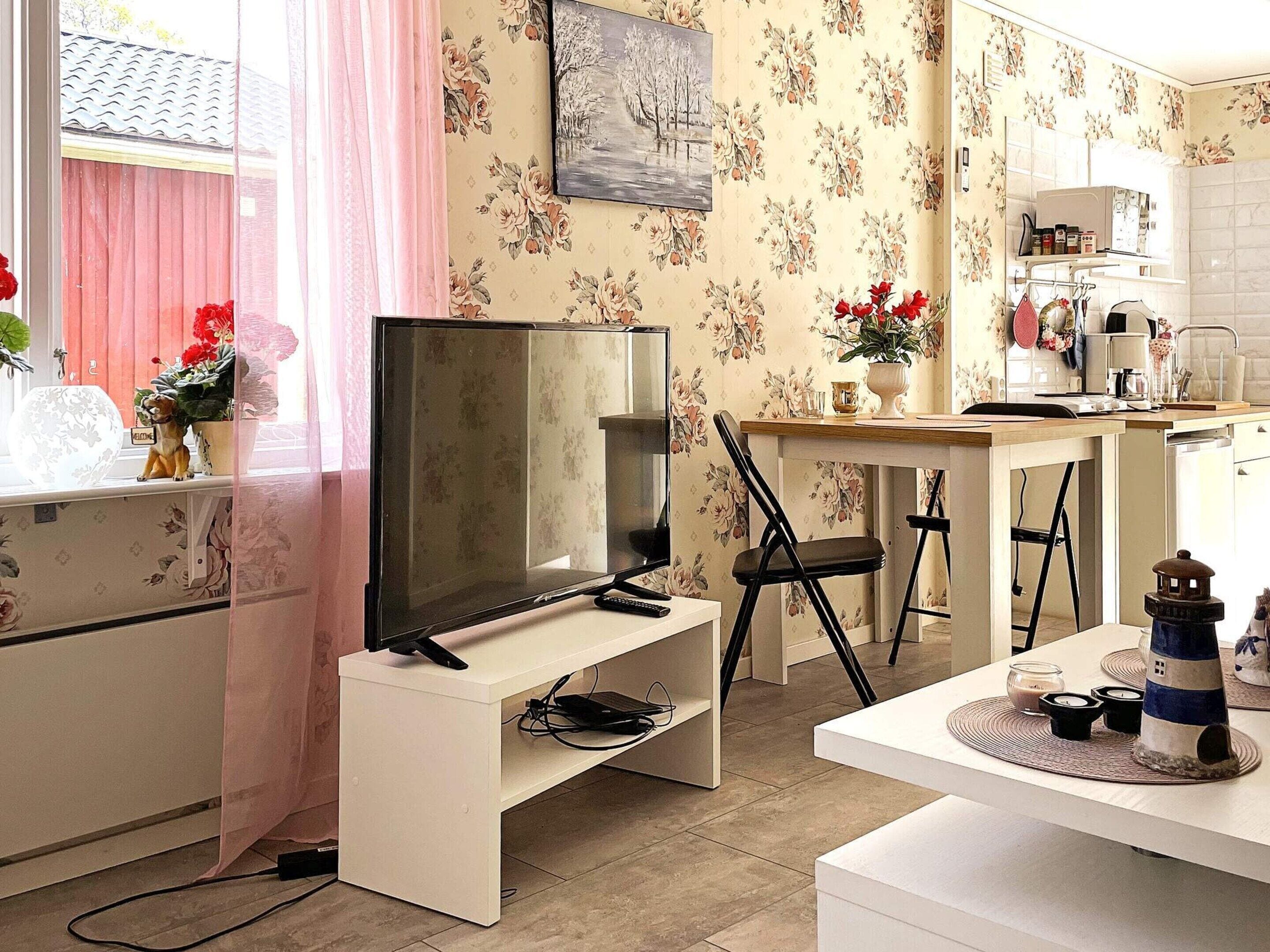 A compact living space with a television on a stand, a dining area with a table and chairs, and a kitchen area with a microwave and other appliances.