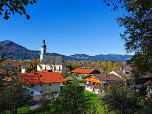 A town with a prominent church featuring a tall tower, surrounded by houses with red roofs, set against a backdrop of mountains and clear blue sky. - Lovely Apartment in Lenggries (Lenggries)