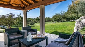 A covered patio area with wicker furniture, a table with a tray, and a view of a grassy landscape. - Villa Casa Ida Comfortable Holiday Residence (Groznjan)