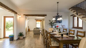 A spacious dining area with a wooden table and chairs, a chandelier, and a view of the garden through the open door. - Villa Casa Ida Comfortable Holiday Residence (Groznjan)