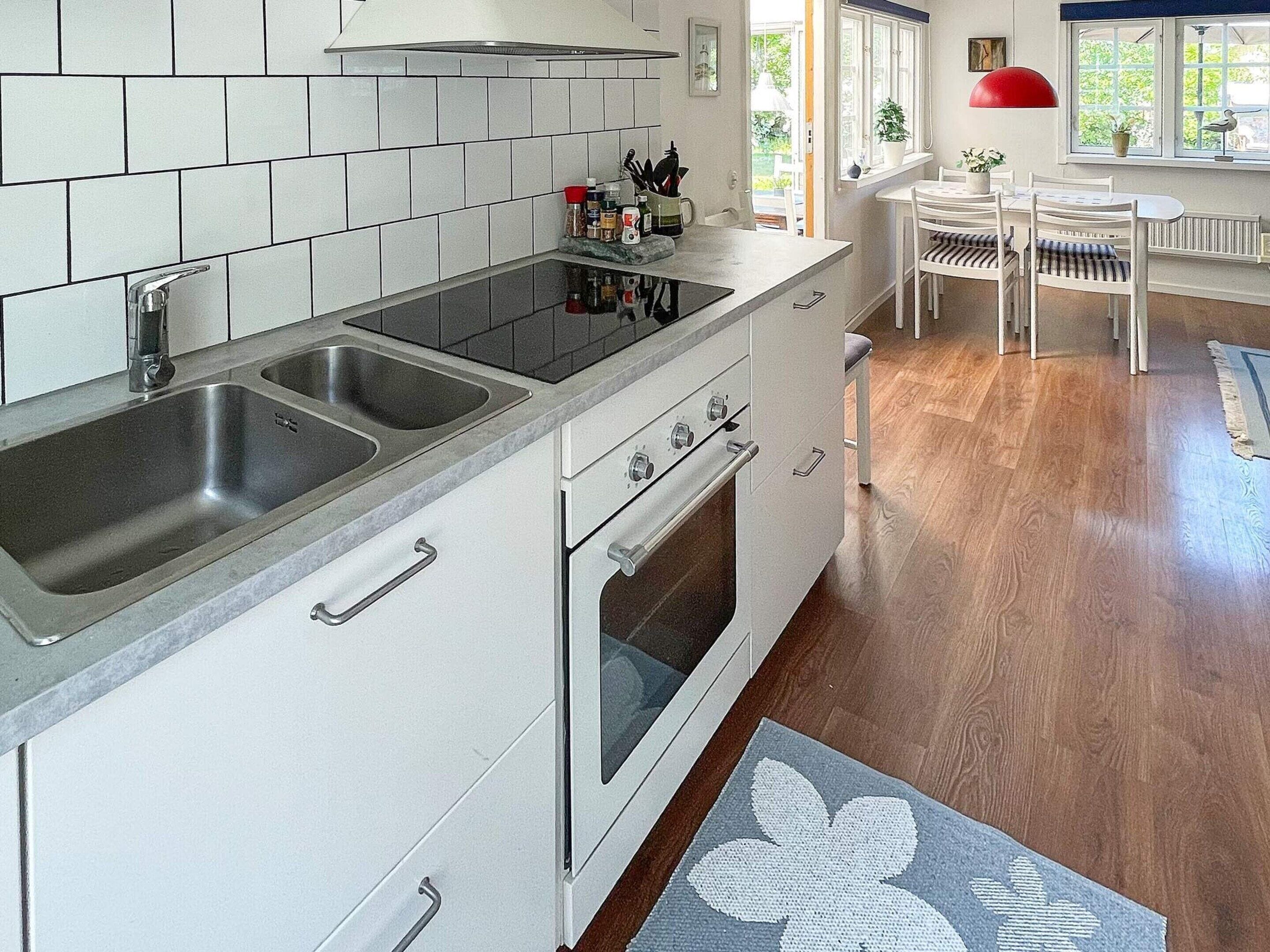 Una cocina moderna con un lavamanos doble, estufa y horno, conectada a un comedor con mesa y sillas.