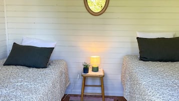 Una habitación con dos camas, una mesita pequeña con una lámpara, un espejo en la pared y suelo de madera.