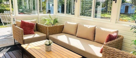 A covered outdoor seating area with a wooden table, cushioned benches, and wicker baskets.
