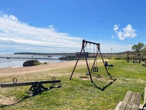 Een park met een schommel, picknicktafels en uitzicht op het water.