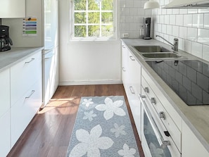 A kitchen with white cabinets, a stainless steel sink, and a window with a view of greenery.