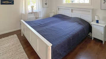 A bedroom with a bed, a nightstand, a window with curtains, and a radiator.