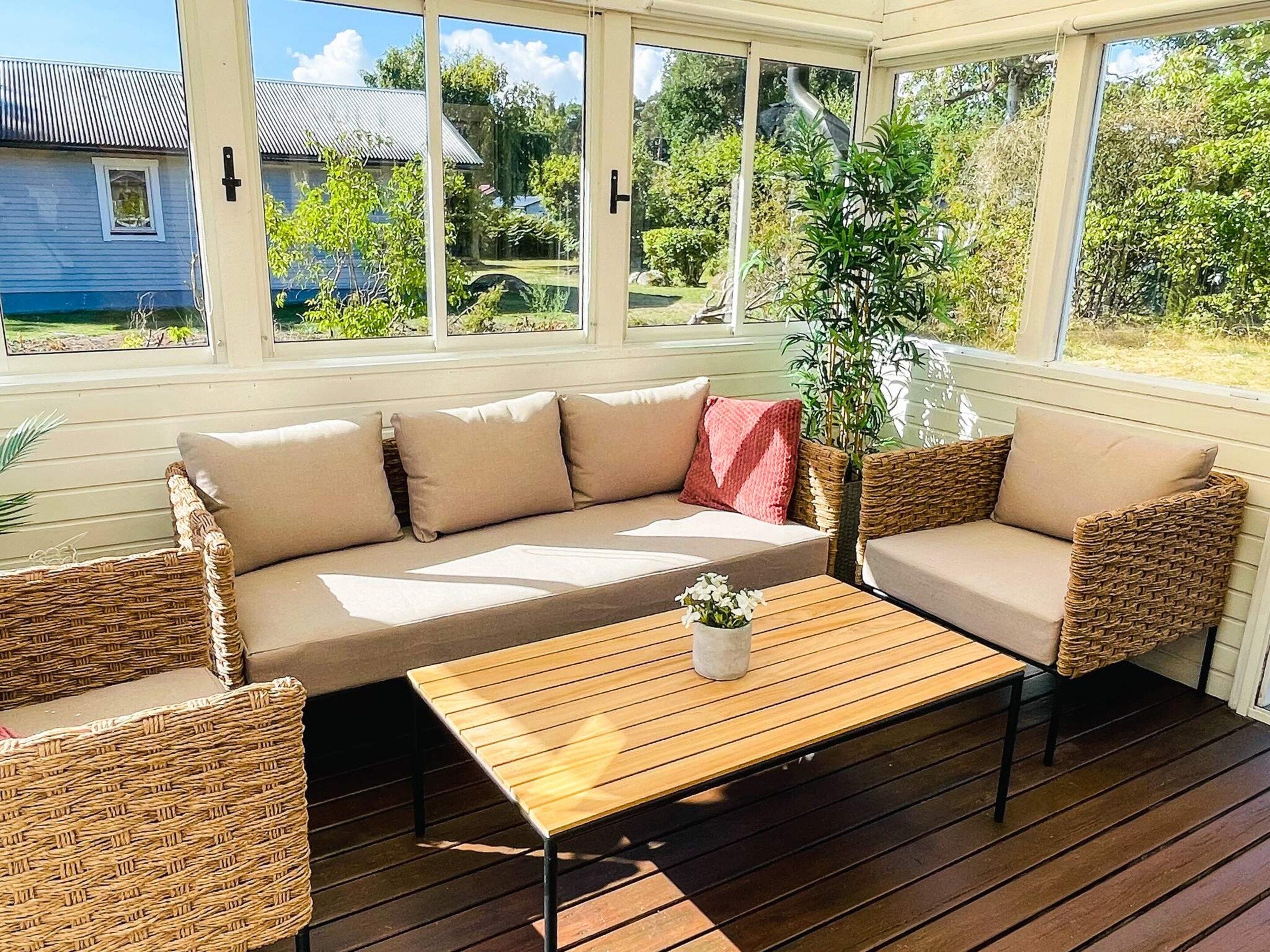 Un espace extérieur aménagé, abrité et doté d’un canapé et de chaises, d’une table en bois et d’une plante en pot.