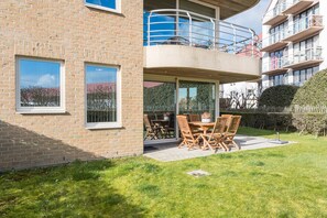 Un edificio a due piani con un balcone, un patio con mobili da esterno e un prato curato.