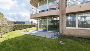 Un bâtiment moderne à deux étages, doté d’un balcon, de grandes fenêtres et d’une cour verdoyante.