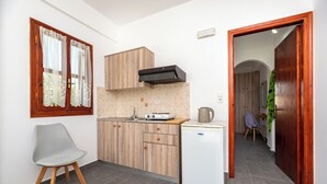 A compact kitchen with wooden cabinets, a small refrigerator, and a window with curtains. - Marina's studios (Santorini)