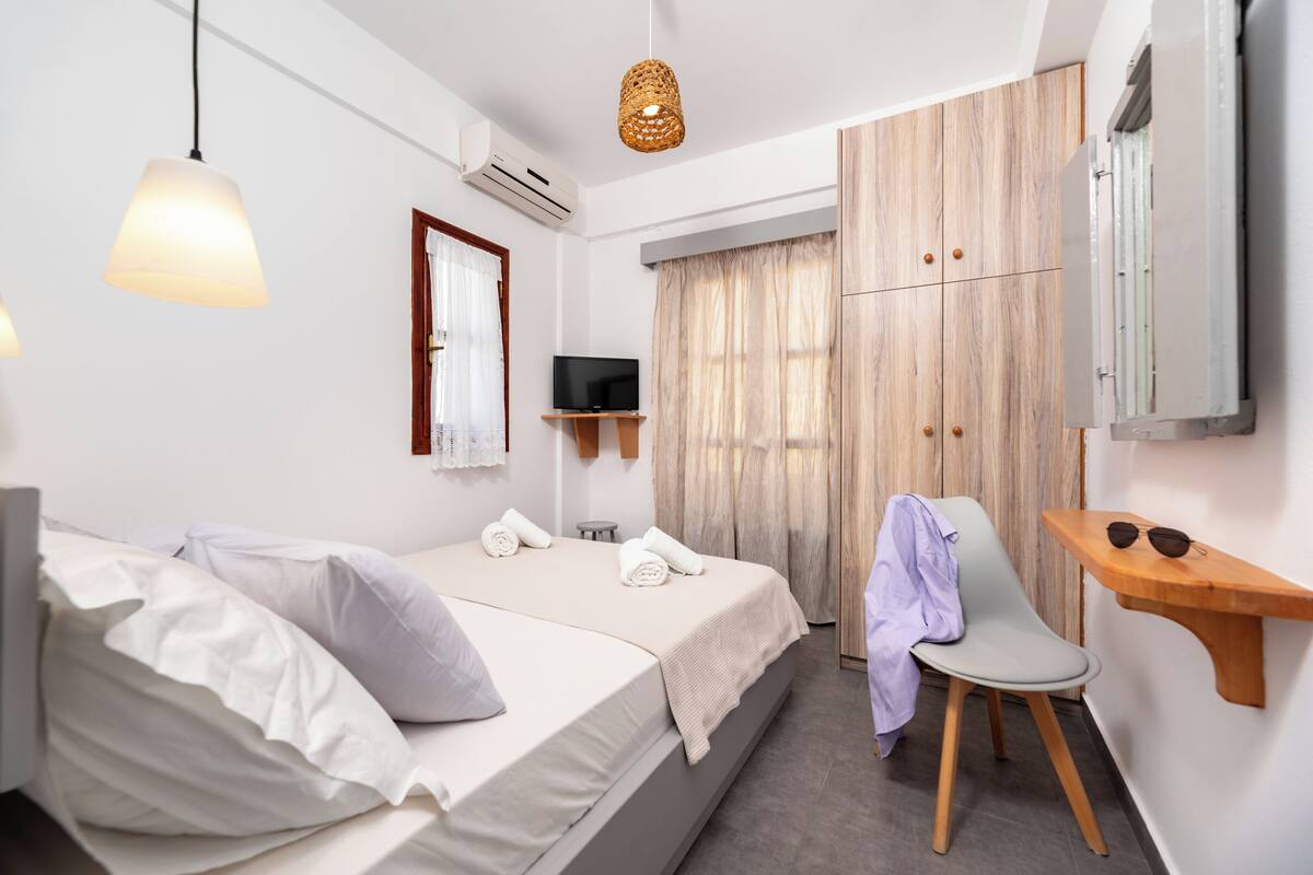 Une chambre d’hôtel avec deux lits, une télévision, une armoire en bois, une chaise et une petite table sur laquelle sont posées des lunettes de soleil.